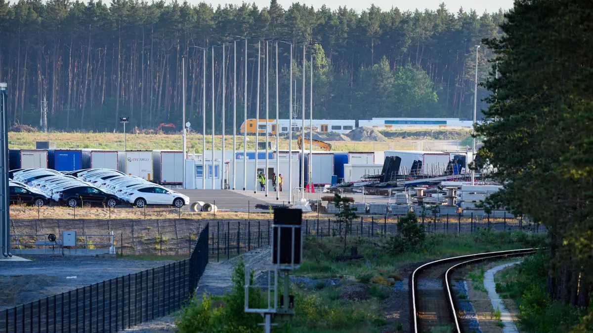 Gleise führen am Waldrand in Richtung des östlichen Teils des Werksgeländes der Tesla Gigafactory. Im Hintergrund fährt ein Regionalzug zum Bahnhof Hangelsberg. Gemeindevertreter von Grünheide hatten am Donnerstagabend einen Bebauungsplan beschlossen, der den Weg für eine Erweiterung des Tesla-Werkes freimacht. Der Autohersteller will sein Gelände um einen Güterbahnhof und Logistikflächen vergrößern. +++ dpa-Bildfunk +++