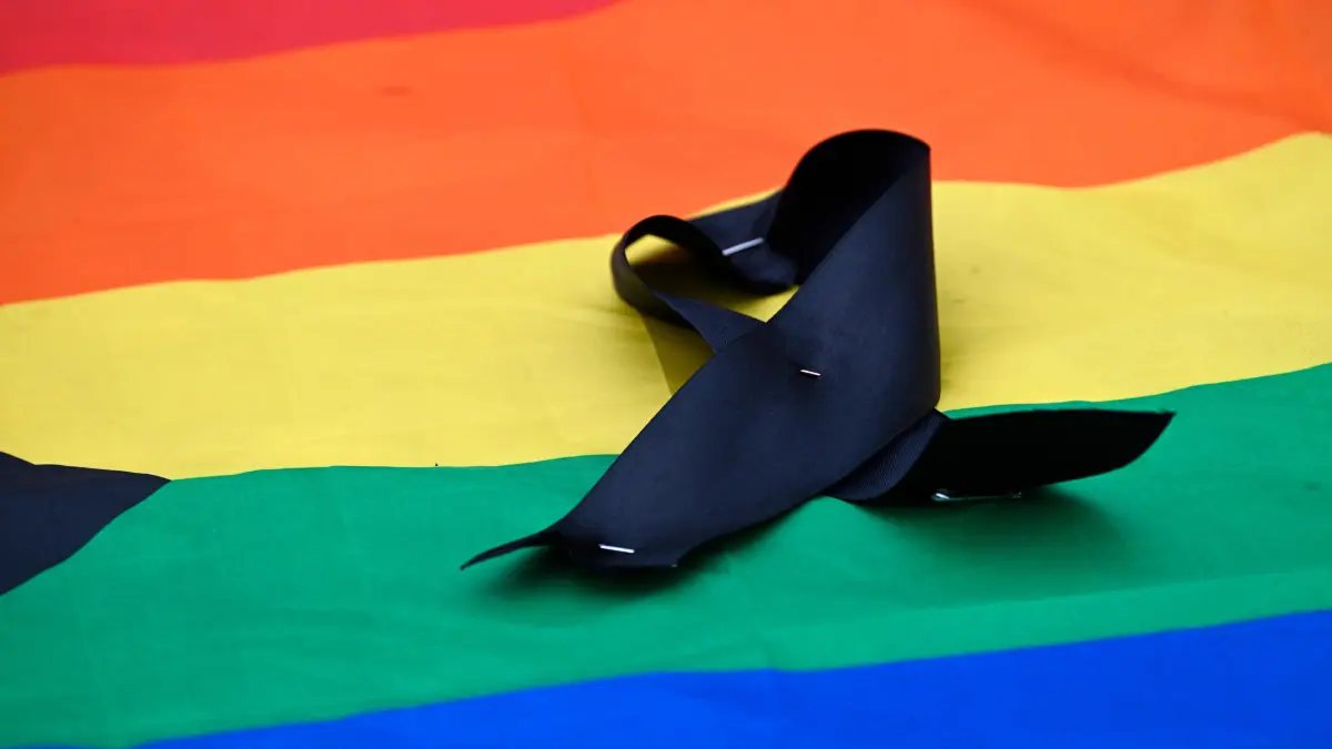 GERMANY-LGBTQ+-PARADE-CSD-POLICE: A black ribbon is placed on a rainbow flag on July 26, 2026 in front of landmark Brandenburg Gate during to a so-called "community mourning" one day after the car ramming attack on people on the outskirts of Berlin's Christopher Street Day (CSD) parade on late July 25, 2026, killing one person and injuring 16 in the Tiergarten park. German police searched on July 26, 2026 for a suspect believed linked to Islamist circles after a car ploughed into a crowd near Berlin's Gay Pride celebrations, killing one person and wounding 16 others. The incident shattered what had been a day of celebration for hundreds of thousands attending Christopher Street Day, one of Europe's largest Pride events, and left revellers fleeing a central Berlin park as sirens echoed through the night. (Photo by RALF HIRSCHBERGER / AFP)