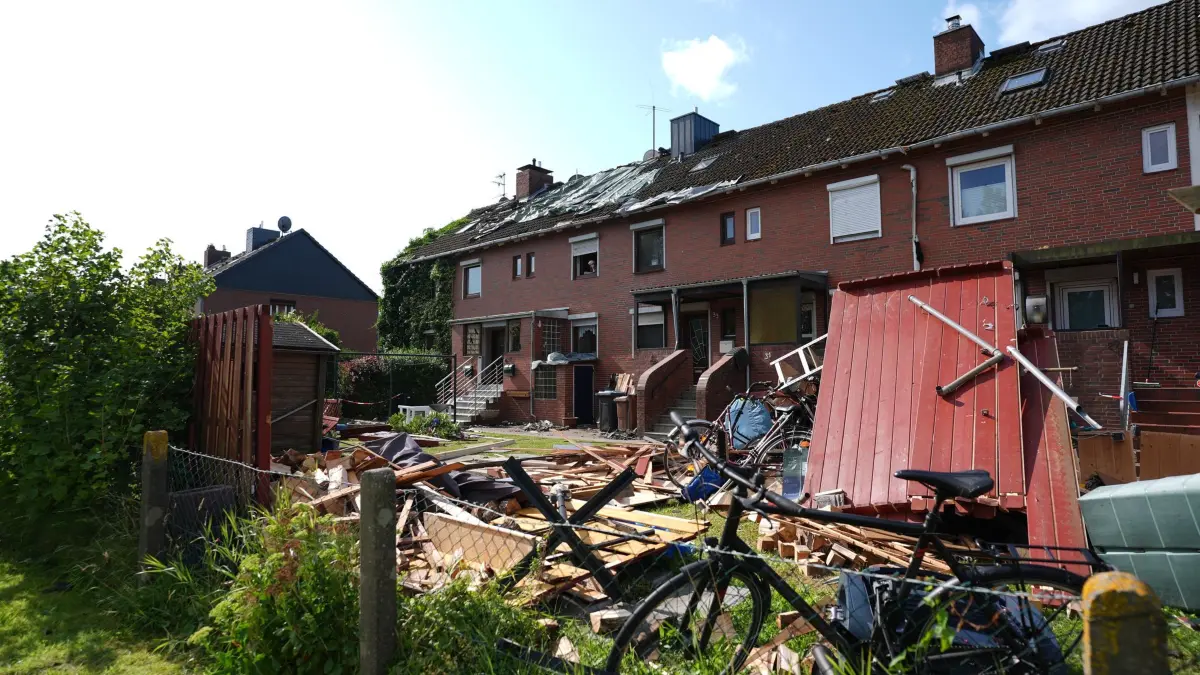 Möglicher Tornado reißt Dächer in Glückstadt ab: 27.07.2026, Schleswig-Holstein, Glückstadt: Provisorische Planen bedecken das durch ein Unwetter abgedeckte Dach eines Reihenhauses. Im Vordergrund liegen Teile einer zerstörten Gartenlaube und Dachziegel. Ein mutmaßlicher Tornado hat in und um Glückstadt in Schleswig-Holstein eine Schneise der Verwüstung geschlagen und nach ersten Schätzungen Schäden in sechs- bis siebenstelliger Höhe verursacht. Dächer wurden abgedeckt, Oberleitungen beschädigt und Gartenhäuser aus ihrer Verankerung gerissen, wie eine Sprecherin der Polizei sagte. (zu dpa: «Tornado beschädigt bis zu 50 Gebäude in Glückstadt») Foto: Marcus Brandt/dpa +++ dpa-Bildfunk +++