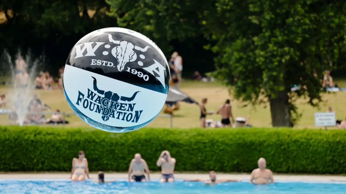 WOA - Wacken Open Air: ARCHIV - 04.08.2022, Schleswig-Holstein, Wacken: Ein aufblasbarer Ball, auf dem das Logo des Wacken Open Air (WOA) zu sehen ist, fliegt im Freibad durch die Luft. Das WOA gilt als das größte Heavy-Metal-Festival der Welt. (zu dpa: «Hitze bei Wacken Open Air - Metalfans im Freibad») Foto: Frank Molter/dpa +++ dpa-Bildfunk +++