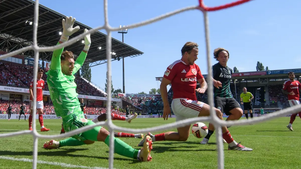 FC Energie Cottbus - Hannover 96: 09.08.2026, Brandenburg, Cottbus: Fußball, Männer: 2. Bundesliga, FC Energie Cottbus - Hannover 96, 1. Spieltag, LEAG Energie Stadion, Torwart Marcel Lotka (FC Energie Cottbus, l), Henry Rorig (FC Energie Cottbus) und Lars Gindorf (Hannover 96, r) kämpfen um den Ball. Foto: Robert Michael/dpa - WICHTIGER HINWEIS: Gemäß den Vorgaben der Bundesliga bzw. des DFB Deutscher Fußball-Bund ist es untersagt, in dem Stadion und/oder vom Spiel angefertigte Fotoaufnahmen in Form von Sequenzbildern und/oder videoähnlichen Fotostrecken zu verwerten bzw. verwerten zu lassen. +++ dpa-Bildfunk +++