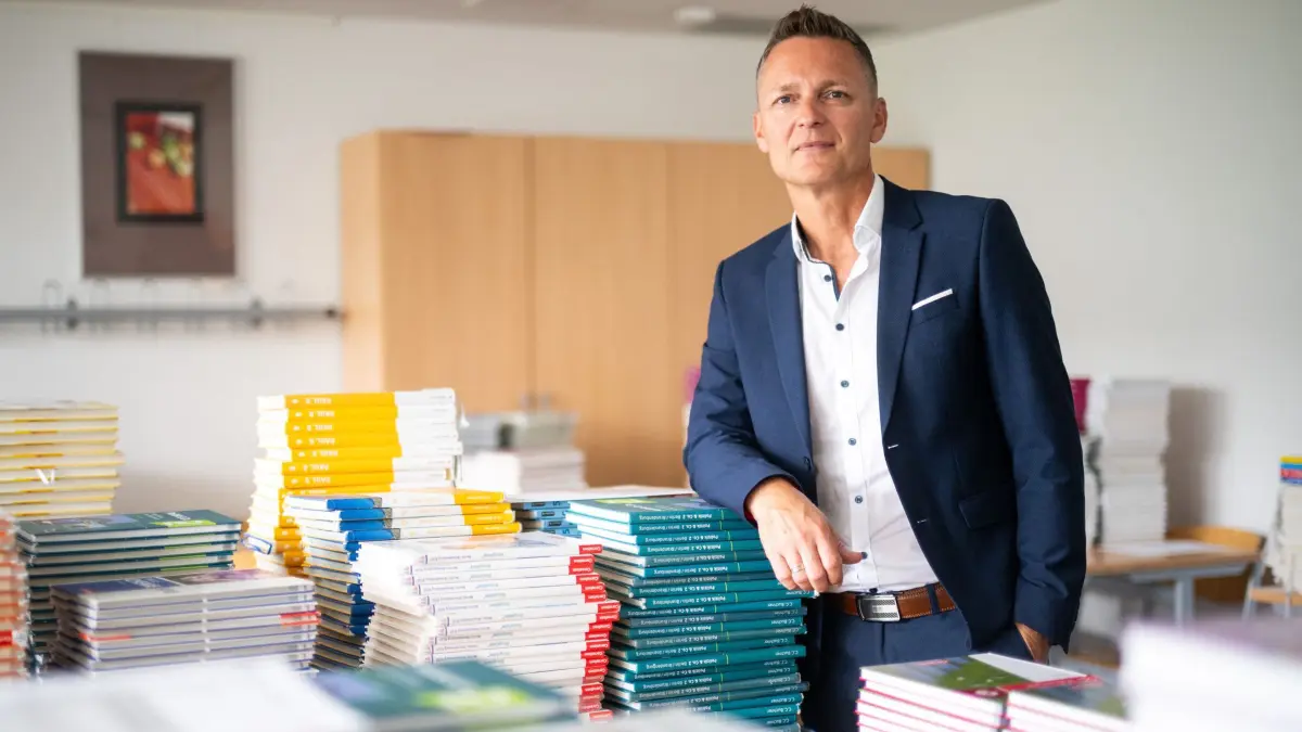 Beginn des Schuljahres 2026/27 in Brandenburg: 19.08.2026, Brandenburg, Cottbus: Mario Kaun, Schulleiter des Ludwig-Leichhardt-Gymnasiums in Cottbus, steht nach einer Pressekonferenz zum Beginn des Schuljahres 2026/27 am Ludwig-Leichhardt Gymnasium in einem Klassenzimmer mit Schulbüchern. Foto: Sebastian Christoph Gollnow/dpa +++ dpa-Bildfunk +++
