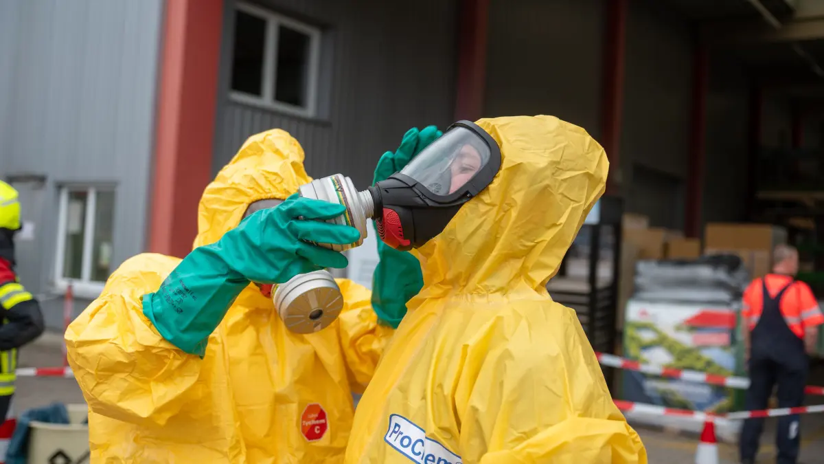 Mit Chemikalienschutzanzügen ausgerüstet sollen die Einsatzkräfte nun den Trupp aus der Lagerhalle dekontaminieren.