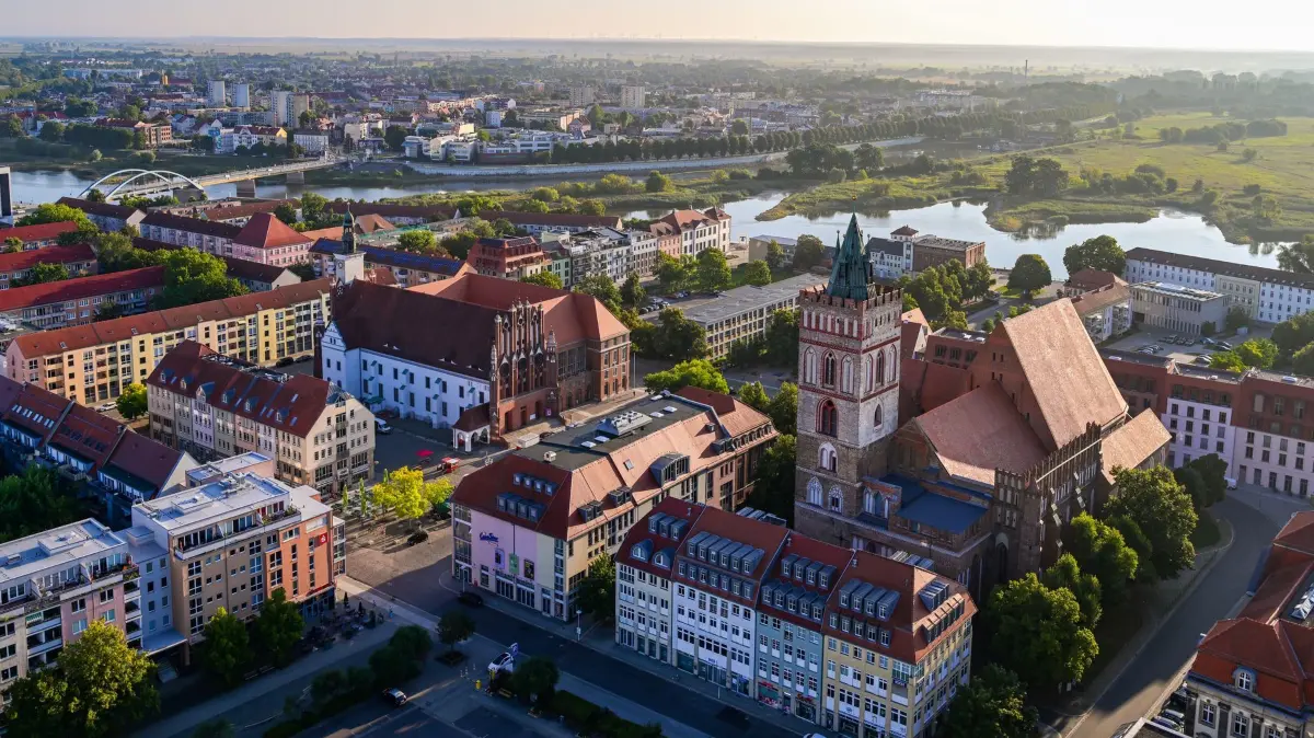Morgenstimmung in Brandenburg: 27.08.2026, Brandenburg, Frankfurt (Oder): Blick am frühen Morgen aus einem Hochhaus über die Dächer der Stadt Frankfurt (Oder) mit dem Rathaus (M), der Marienkirche (r), sowie dem deutsch-polnischen Grenzfluss Oder und der polnischen Stadt Slubice im Hintergrund. Nach freundlichem Wetter drohen laut DWD im Wochenverlauf kräftige Schauer und Gewitter in der Region. Foto: Patrick Pleul/dpa - Honorarfrei nur für Bezieher des Dienstes ZB-Funkregio Ost +++ ZB-FUNKREGIO OST +++