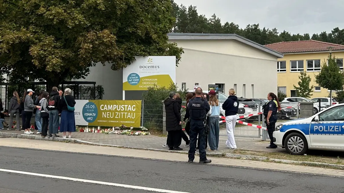 Docemus-Campus in Neu Zittau: Menschen, darunter Schüler und Angehörige, bringen Blumen und Kerzen zum Gedenken an die Opfer zum Eingang einer Schule in Gosen-Neu Zittau. Bei der Gewalttat wurden am Donnerstag eine Frau und ein Mann getötet.