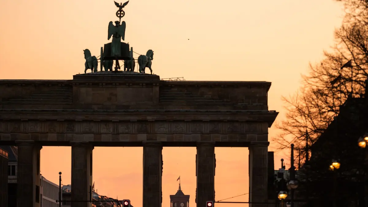 Berlin: ARCHIV - 28.02.2026, Berlin: Hinter dem Brandenburger Tor in Berlin färbt sich der Himmel bei Sonnenaufgang rötlich. (zu dpa: «Umfrage: Mehrheit sieht Wiedervereinigung als Glücksfall») Foto: Christophe Gateau/dpa +++ dpa-Bildfunk +++