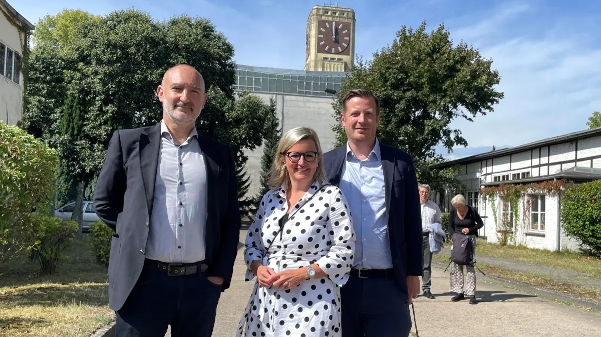 Investor Renaud Vercouter (links) mit der brandenburgischen Wirtschaftsministerin Martina Klement (CSU). Rechts neben Klement steht Christian Woronka, Geschäftsführer der TMB Tourismus-Marketing Brandenburg GmbH. Im Hintergrund ist der berühmte Uhrenturm des Nähmaschinenwerkes zu sehen.
