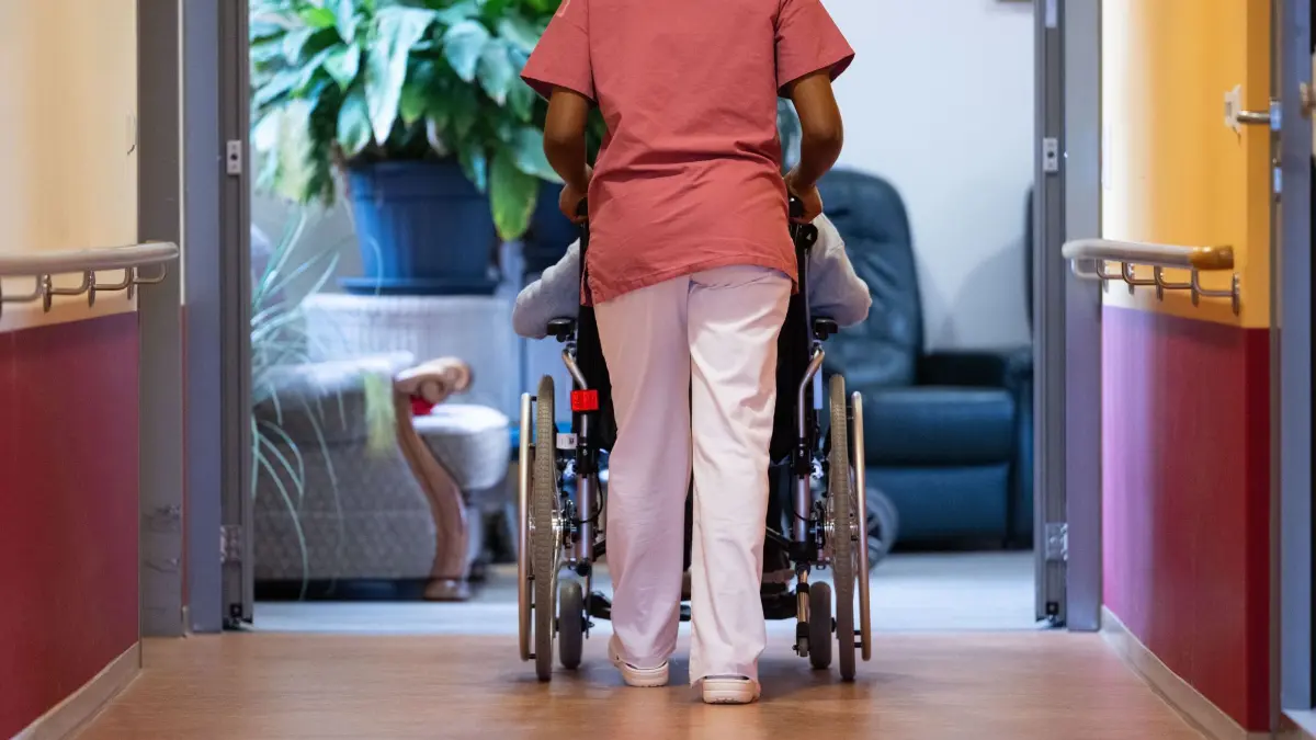 Pflegerin und Patientin (Symbolbild): ARCHIV - 07.02.2024, Baden-Württemberg, Filderstadt: Eine Bewohnerin eines Pflegeheims wird von einer Pflegerin einen Gang entlang geschoben. (zu dpa: «Rehlinger will Eigenanteil für Pflegeheim-Platz deckeln») Foto: Marijan Murat/dpa +++ dpa-Bildfunk +++