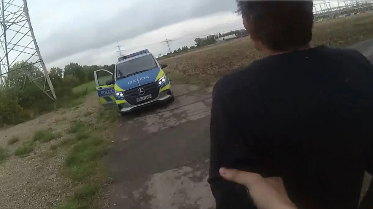 Festnahme Strom-Saboteur: HANDOUT - 10.09.2026, Nordrhein-Westfalen, Weisweiler: Die Bodycam eines Autobahnpolizisten zeigt wie das Versteck des tatverdächtigen Strom-Saboteurs gefunden und er verhaftet worden ist. Die Aufnahmen zeigen, wie die beiden jungen Beamten der Spur im Gras folgen und im Gebüsch rund 200 Meter neben dem Weg auf einen Mann stoßen. Ein Polizist zieht seine Pistole, fordert den Mann auf, sich auf den Boden zu legen. Der leistet keinen Widerstand und folgt allen Anweisungen. Tagelang hatten die Angriffe auf das Stromnetz in Nordrhein-Westfalen, Brandenburg und Sachsen für Schlagzeilen in den Medien und einen Großeinsatz der Polizei gesorgt. Foto: --/Polizei Nordrhein-Westfalen/dpa - ACHTUNG: Nur zur redaktionellen Verwendung im Zusammenhang mit der aktuellen Berichterstattung und nur mit vollständiger Nennung des vorstehenden Credits +++ dpa-Bildfunk +++