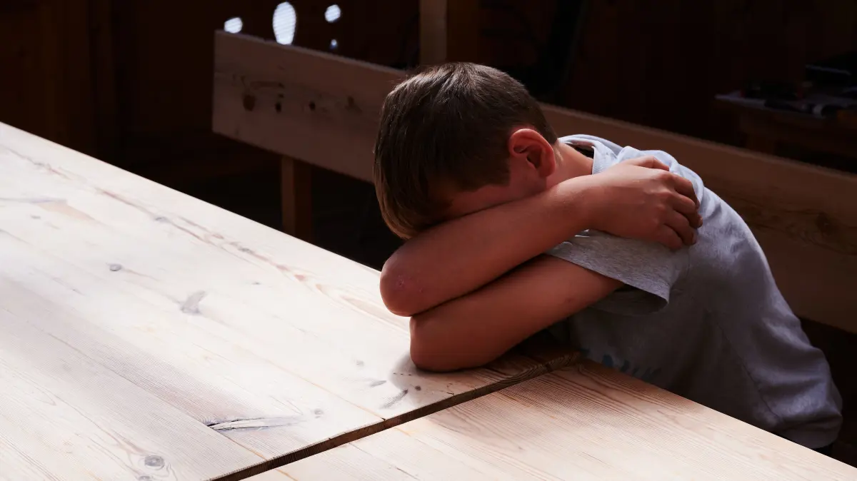 ILLUSTRATION - Ein Kind versteckt sein Gesicht unter seinen Armen und liegt mit dem Kopf auf einem Tisch. (gestellte Szene) Jeder zweite Mensch in Deutschland hat in der Kindheit oder Jugend körperliche Gewalt erfahren. Das zeigt eine von der Bundesregierung in Auftrag gegebene große Studie. (zu dpa: «Mehr als jeder Zweite hat als Kind körperliche Gewalt erlebt») +++ dpa-Bildfunk +++