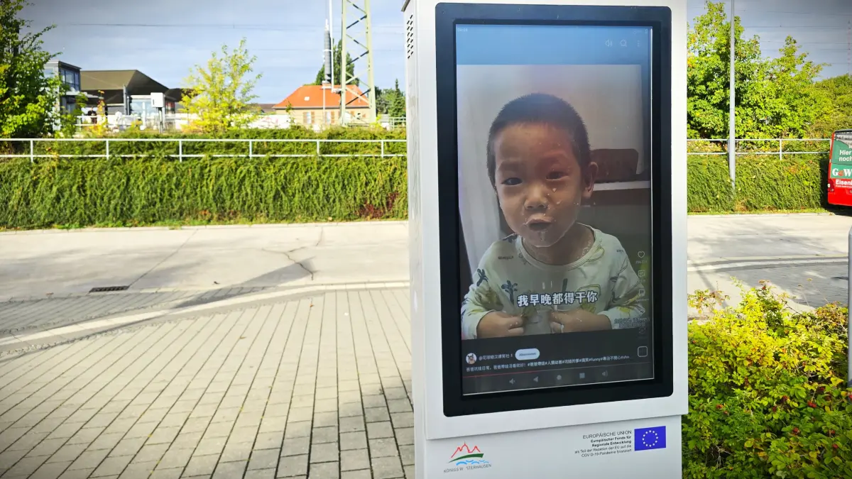 Ein Video-Screen der Stadt Königs Wusterhausen auf der Ostseite des Bahnhofs, zeigt ein Kind und Asiatische Schriftzeichen.