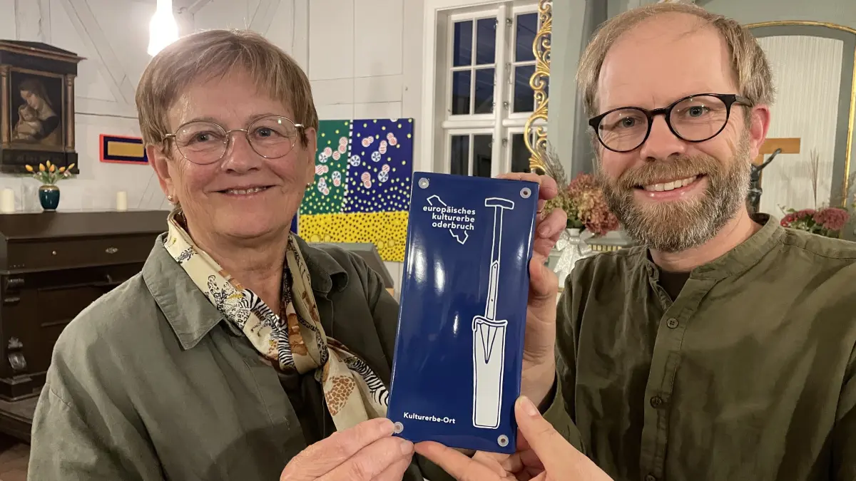 Mit neuem Schild: Den Vertretern der mehr als 40 Kulturerbestätten im Oderbruch hat Koordinator Tobias Hartmann die jetzt dunkelblauen Plaketten ausgereicht. Gudrun Wendt hat sie für den Kirchenförderverein Altwriezen entgegengenommen.