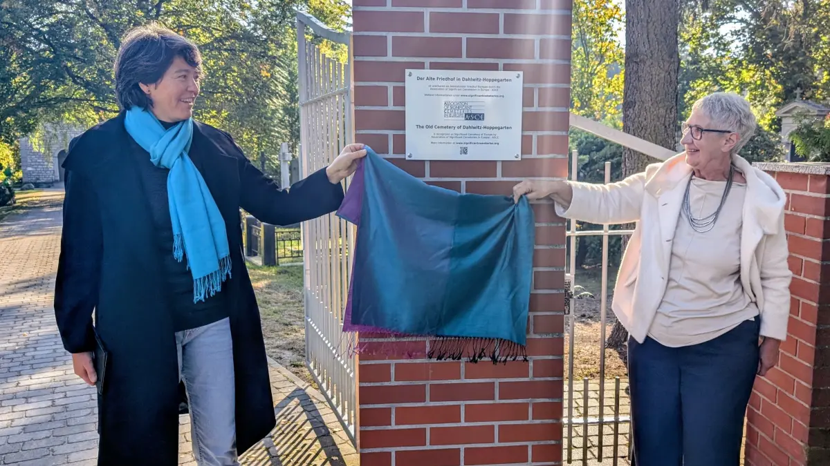 Valérie Madoka Naito (links) von der Vereinigung bedeutender Friedhöfe in Europa (ASCE) und Astrid Fritsche vom Kulturverein „Grünes Tor“ Hoppegarten enthüllen eine Tafel am Alten Friedhof Dahlwitz.