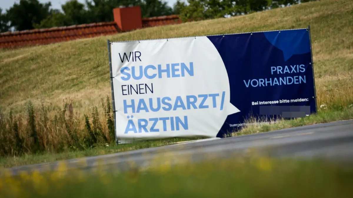 Warten auf den Nachfolger: Hausärzte werden in Brandenburg noch essenzieller für die medizinische Versorgung und gleichzeitig nimmt ihre Zahl ab. Mit vereinten Kräften will man nun mehr Ärzte für die Allgemeinmedizin gewinnen, spart aber an anderer Stelle. (Symbolfoto) ARCHIV - 12.07.2022, Schleswig-Holstein, Friedrichskoog: Ein Plakat mit dem Text «Wir suchen einen Hausarzt / Ärztin - Praxis Vorhanden» steht am Ortseingang. Hausärzte werden in vielen ländlichen Regionen gesucht. (Zu dpa «Medizinstudenten lernen auf dem Land, um zu bleiben») Foto: Christian Charisius/dpa +++ dpa-Bildfunk +++