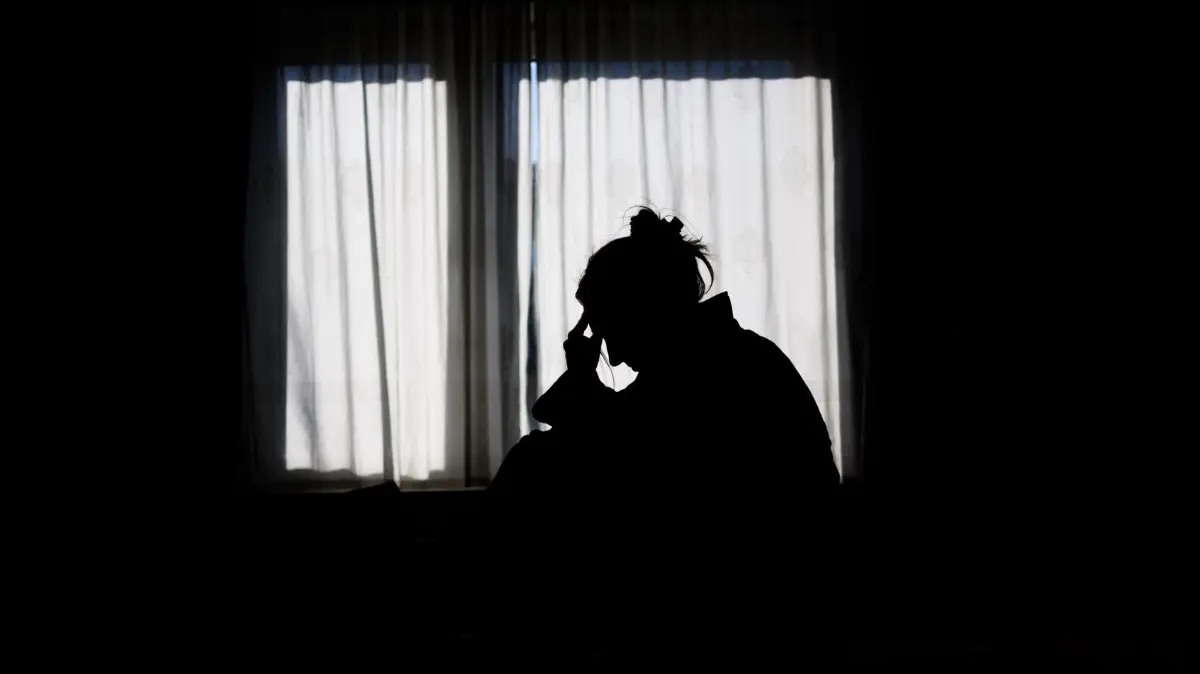 Symbolbild Einsamkeit: ILLUSTRATION - Die Silhouette einer Frau zeichnet sich vor einer hellen Fensterfront ab (gestellte Szene). (zu dpa: «Sozialminister Wilke würdigt Arbeit der Telefonseelsorge»)
