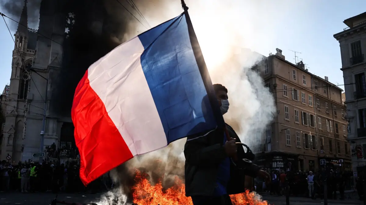 Protesttag in Frankreich: Ein Demonstrant, der eine französische Nationalflagge schwenkt, geht während Zusammenstößen vor Beginn einer Demonstration gegen die „hohen Lebenshaltungskosten“ an einem Feuer vorbei. Die Aktion ist Teil eines landesweiten Mobilisierungsaufrufs, der verschiedene Gruppen zusammenbringt. (zu dpa: «Bilder des Tages»)
