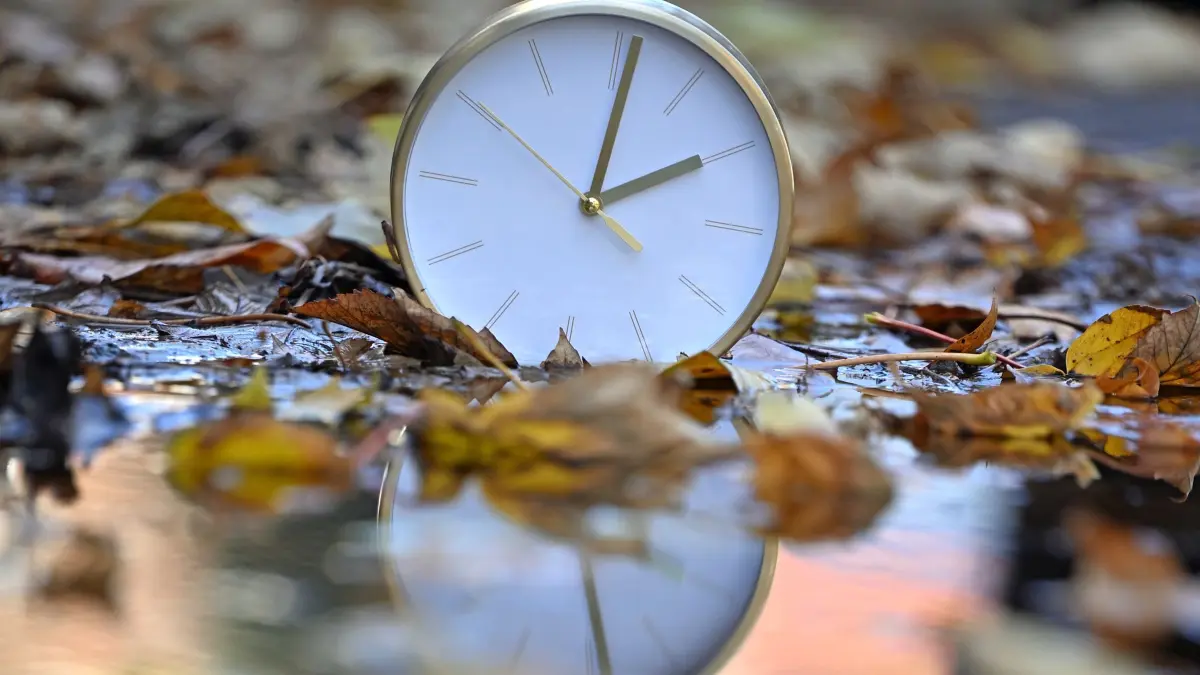 Zeitumstellung: ARCHIV - 21.10.2025, Sachsen, Leipzig: Eine Uhr spiegelt sich im blätterbedeckten Wasser. Mit Beginn der Winterzeit werden in Deutschland und den meisten anderen Ländern Europas am Sonntagmorgen (25. Oktober) die Uhren von 3.00 Uhr auf 2.00 Uhr zurückgestellt. (zu dpa: «Barmer: Thüringer besonders betroffen von Schlafproblemen») Foto: Jennifer Brückner/dpa +++ dpa-Bildfunk +++